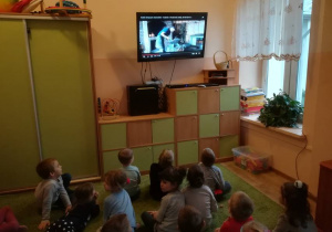 Dzieci w sali telewizyjnej oglądają film, na którym widać jak kowal wykonuje podkowę.